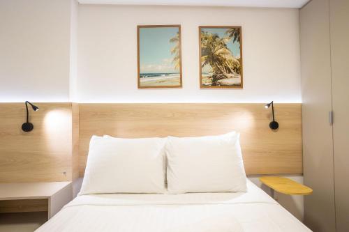 a bedroom with a white bed with three pictures on the wall at Oceânica Cabo Branco By Carpediem in Tambaú