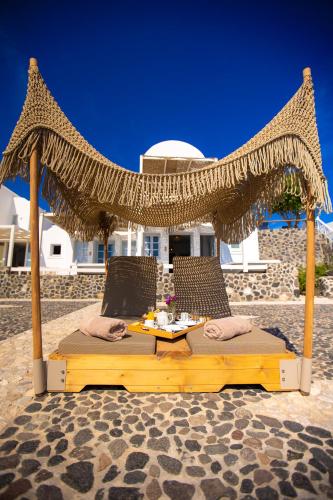 a table and two chairs under a straw umbrella at Phaos Santorini Suites in Imerovigli