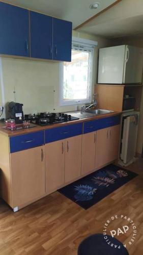 une cuisine avec des armoires bleues, un évier et une fenêtre dans l'établissement Le gazon de ronce, à La Tremblade