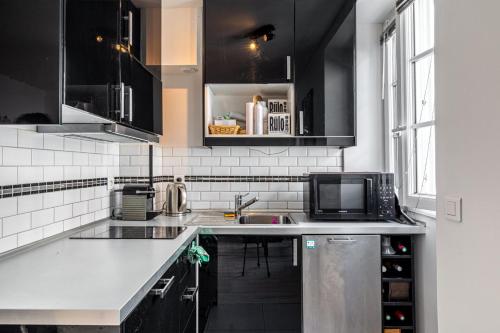 une cuisine avec des armoires noires et un comptoir blanc dans l'établissement GuestReady - Charming Canal St-Martin Retreat, à Paris