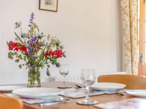 a table with a vase of flowers and glasses on it at Swallow's Nest in Craven Arms