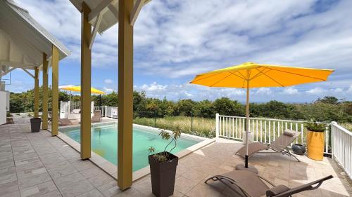 a patio with an umbrella and chairs and a pool at Villa Boréale in Capesterre-de-Marie-Galante