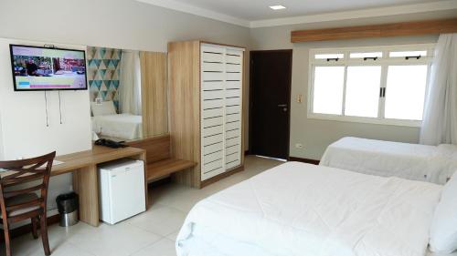 a bedroom with a bed and a desk and a television at Hotel Costa Norte Massaguaçu in Caraguatatuba