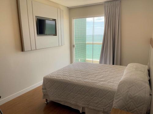 a bedroom with a bed and a window with a television at Hotel Plaza Mar in Vila Velha