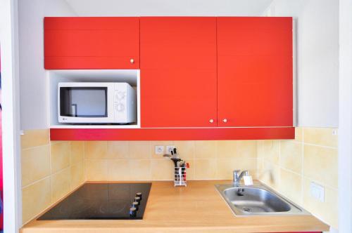 La cuisine est équipée de placards rouges, d'un évier et d'un four micro-ondes. dans l'établissement La résidence du Lac - maeva Home - Appartement 2 pièces 5 personnes - Sélection MAE-5694, à Monflanquin