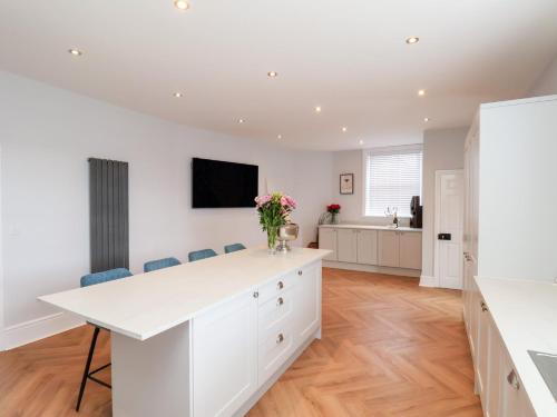 a white kitchen with a white counter and blue chairs at Harpham Manor House in Lowthorpe
