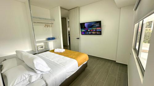 a bedroom with a white bed and a tv at Hotel PAUCHÉ Topiario Zapatoca in Zapatoca