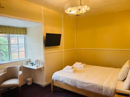 a yellow room with a bed and a chair and a television at Rothwell House Hotel in Kettering