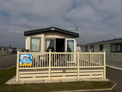 a tiny house with a porch and a fence at Golden Palm Resort - The Haywood - Coastal Caravan Breaks in Chapel Saint Leonards