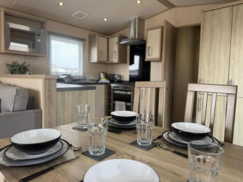 a dining room table with plates and glasses on it at Golden Palm Resort - The Haywood - Coastal Caravan Breaks in Chapel Saint Leonards