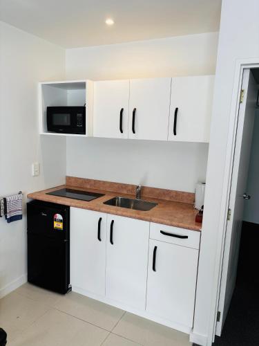 a kitchen with white cabinets and a sink and a microwave at Bush Inn Court Motel in Christchurch