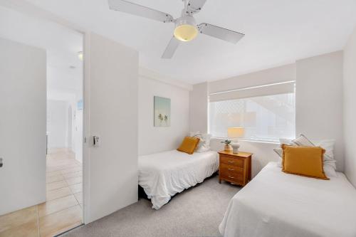 two beds in a white room with a ceiling fan at Headlands 10 Two Bedroom Beachside Apartment with Magical Ocean Views Great Value for Money in Alexandra Headland