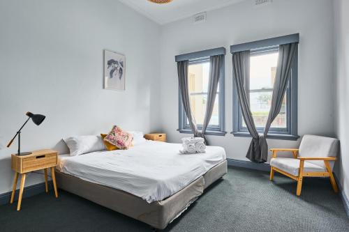 a bedroom with a bed and a chair and windows at College Lawn Hotel in Melbourne