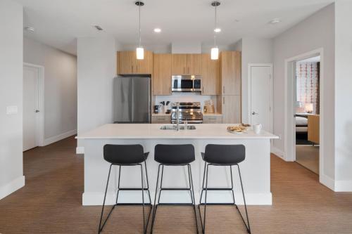 a kitchen with a white island with three bar stools at Luxury Apartments by Hyatus Boston Somerville in Somerville