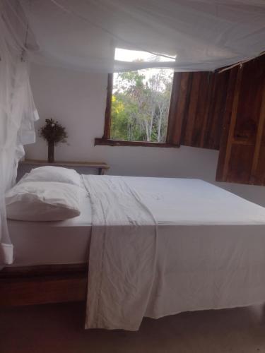 un letto bianco in una camera da letto con finestra di Hostel Mata House Nova Caraíva a Porto Seguro