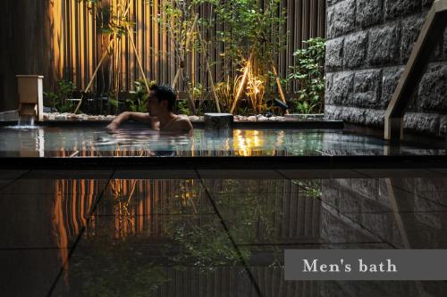 a man in a jacuzzi tub in a garden at ONSEN RYOKAN Yuen Sapporo in Sapporo