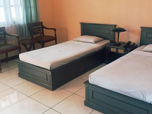two beds in a bedroom with two chairs and a phone at Hotel Wijaya Purwokerto in Purwokerto