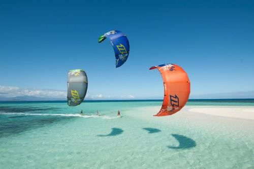 three kites flying over the water on a beach at Windtown Lagoon Hotel in Langebaan
