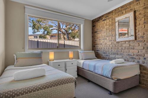 two beds in a bedroom with a brick wall at Lakeside Apartments - Fishpen in Merimbula