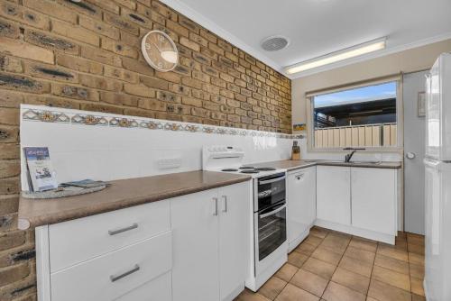 a kitchen with white cabinets and a brick wall at Lakeside Apartments - Fishpen in Merimbula