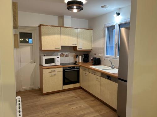 La cuisine est équipée de placards en bois, d'un évier et d'un four micro-ondes. dans l'établissement Charmante maison, à Jard-sur-Mer
