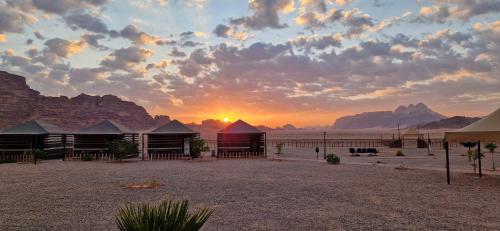 a sunset over a desert with a group of buildings at Dream Bedouin Life Camp Wadi Rum in Disah