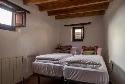 two beds in a room with wooden ceilings at Casa Walhalla & Cortijo El Páramo in Pampaneira