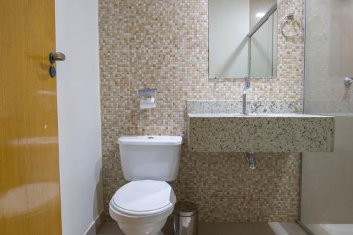 a bathroom with a toilet and a sink and a mirror at OYO Tropical Confort Hotel, Brasilia in Brasilia