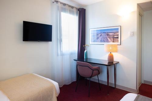 a room with a desk and a bed and a window at Hôtel les jardins du canal - piscine chauffée - parking - garage - bornes électriques in Aigues-Mortes