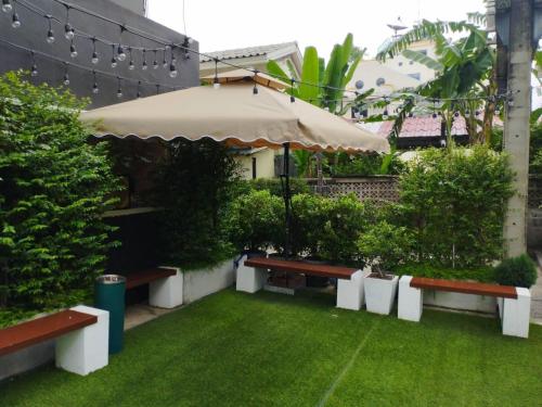 a patio with benches and an umbrella and grass at OYO 75446 Travis Inthamara 49 in Bangkok