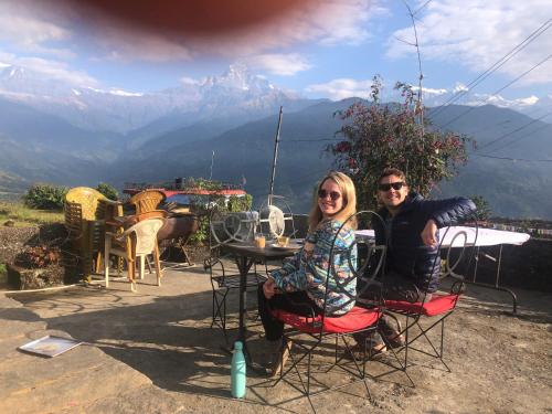 a man and a woman sitting at a table with mountains in the background at Anne Homestay in Pokhara