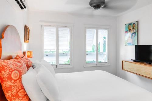 a white bedroom with a bed and two windows at Plantation House Trinidad suite in Playa del Carmen
