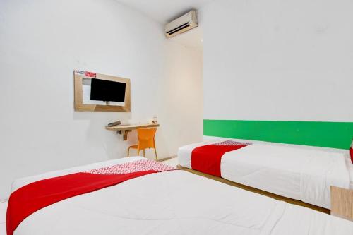 two beds in a room with a desk and a tv at Collection O Jalan Slamet Riyadi Near Kampung Batik Kauman Formerly Hotel Grand Kota in Solo