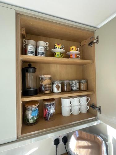 a cupboard with cups and mugs in a kitchen at 2025 Traveller award winner Just bring clothes in West Kirby