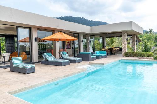 a pool with chairs and an umbrella next to a house at White Monkey Villa - Private Pool & Jacuzzi in Pantai Cenang