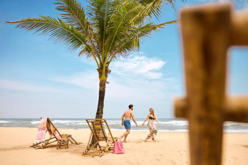 a man and woman walking on the beach with a palm tree at ROBINSON Nam Hoi An in Tam Ky
