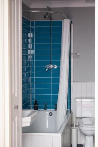 a blue tiled bathroom with a tub and a toilet at 7 Crown Gardens Glasgow in Glasgow