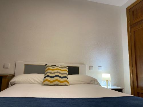a bed with a yellow and blue striped pillow on it at Hostal La Trucha Sanabria in Puebla de Sanabria