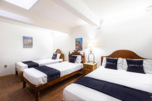 three beds in a room with white walls at Capital O Posada La Casa De La Tia, Oaxaca in Oaxaca City