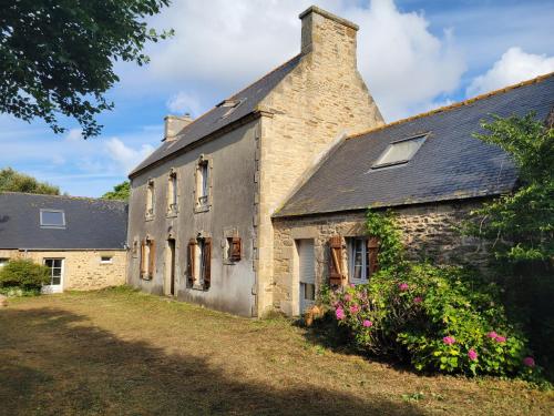 an old stone house with a chimney and flowers at Ancienne ferme bord de mer in Plozévet