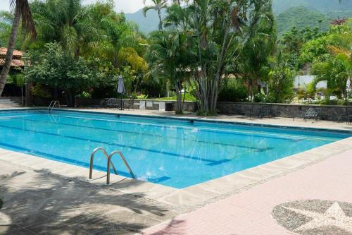 a large blue swimming pool with trees and mountains in the background at Capital O La Joya Del Lago in Ajijic
