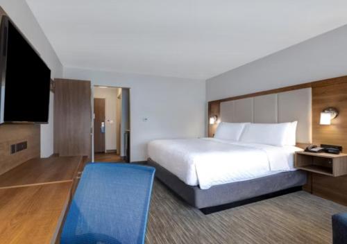 a hotel room with a bed and a blue chair at Holiday Inn Express & Suites - Detroit - Dearborn by IHG in Dearborn