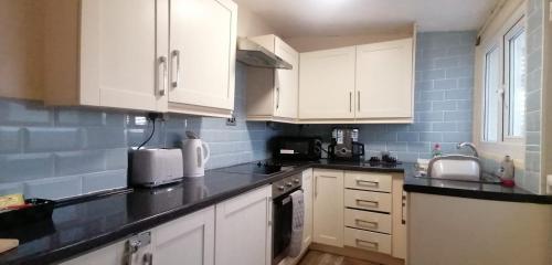 a kitchen with white cabinets and black counter tops at Birchwood Apartment in Llandudno