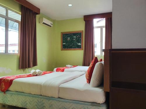 two beds in a room with green walls and windows at Hotel O Melody 88 Inn in Miri