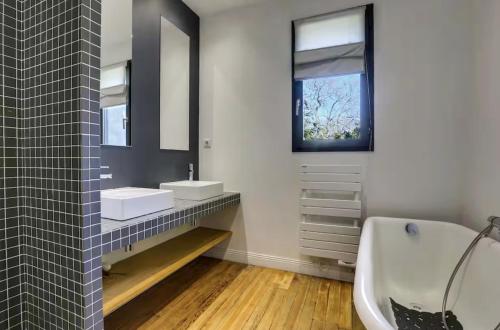 une salle de bain avec deux lavabos, une baignoire et un miroir dans l'établissement Maison Biarritz, à Biarritz