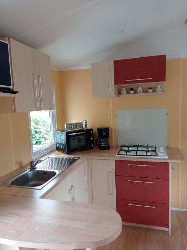 une petite cuisine avec des armoires rouges et un évier dans l'établissement Charming Mobile Home Campsite 3stars 40 min from Paris, à Saint-Chéron