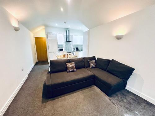 a black couch in a living room with a kitchen at Stylish 1 Bedroom Flat in the Heart of Staines in Staines upon Thames