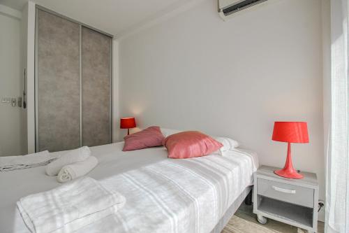- un lit blanc avec des oreillers roses et une lampe rouge dans l'établissement CHENES Lumineux Vue Mer Clim Confort Terrasses Parking, à Antibes