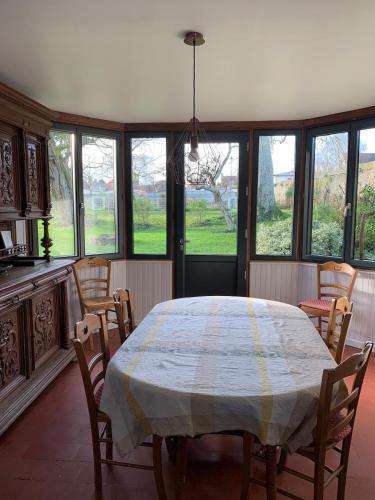 une salle à manger avec une table, des chaises et des fenêtres dans l'établissement Grande maison proche des plages du débarquement, à Colleville-Montgomery