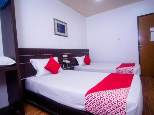 two beds in a hotel room with red pillows at Hotel O Mayfair Hotel in Kuching